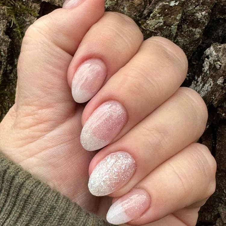 Ovale Nägel mit rosa-weißem Glitzerverlauf vor Baumrinde